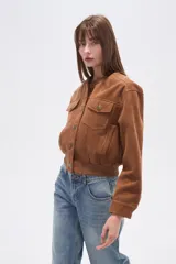 Campera estilo bomber corta de gamuza color marrón, con cuello redondo, cierre frontal de botones y dos bolsillos de parche con solapa en el pecho. Presenta puños y cintura elásticos.