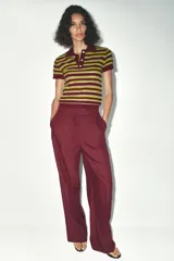 Pantalón de vestir color borgoña, de tiro alto y pierna ancha, con bolsillos laterales y cierre frontal con cremallera y ganchos metálicos.