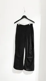 Pantalón negro con detalles de pinzas en la rodilla, diseño holgado.