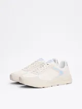 Zapatillas deportivas Tommy Hilfiger de corte bajo, color blanco con detalles en celeste y plateado. Presentan paneles de malla y superposiciones de gamuza, con el monograma TH en la lengüeta y el lateral.