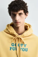 Sudadera con capucha color ocre, de corte holgado y mangas largas. Estampado frontal con texto en azul.