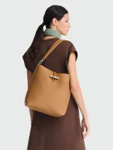 Bolso tipo hobo de cuero color caramelo, con correa de hombro ajustable y cierre de broche metálico.