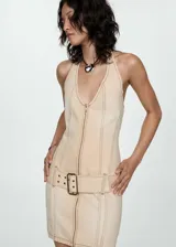 Minivestido de jean color beige, con cuello halter, cierre frontal con cremallera y cinturón con hebilla.