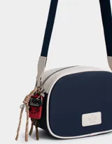 Bandolera de cuerina azul marino y beige con correa regulable azul y charm lateral decorativo. Tiene cierre superior y tag frontal con logo "The Brunch Club".