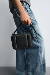 Bandolera negra acolchada con correa ajustable. Tiene un compartimento principal con cierre de cremallera, un bolsillo plano interior y tres compartimentos para tarjetas.