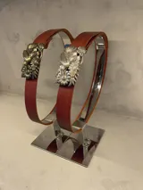 Cinturón de cuero color bordó con hebilla de metal dorada con diseño de flores y pájaros.