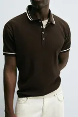 Polo color crema de punto canalé con cuello solapa, cierre frontal de botones a presión y manga corta con ribete a contraste en negro.
