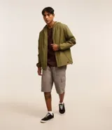Campera rompevientos color verde oliva, con capucha ajustable con cordón, cierre frontal con cremallera, bolsillos laterales con cremallera y puños elásticos.