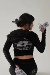 Conjunto deportivo negro de terciopelo con ribetes rosados, compuesto por un hoodie crop con cierre y un pantalón de corte amplio con estampado de logo en la pierna.