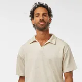 Remera tipo polo color beige claro, de manga corta y corte holgado.