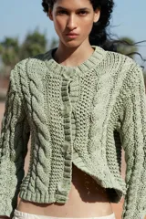 Chaqueta de punto color verde claro, con cuello redondo y manga larga. Cierre frontal con botones a presión en forma de flor.