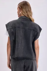 Chaleco de jean negro con cuello camisero, cierre frontal con botones, bolsillos de parche y sisas desflecadas.
