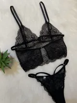 Conjunto de lencería negro de encaje, compuesto por un corpiño tipo top con breteles regulables, espalda con tiras y cierre trasero con gancho, y una tanga regulable con corte medialess.