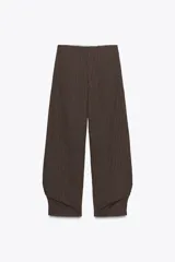 Pantalón de tiro medio confeccionado en hilatura con mezcla de lino a rayas verticales marrones y blancas. Presenta bolsillos laterales ocultos en costura, detalle de pliegues en el bajo y cierre frontal con cremallera, botón y ganchos metálicos.