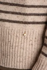 Sweater de lana y nylon, color beige jaspeado con rayas horizontales marrones oscuras. Presenta cuello alto con abertura frontal abotonada con tres botones marrones.