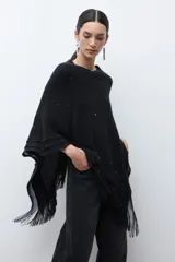 Capa tejida color negro, con cuello redondo, diseño de punto y detalles de lentejuelas. Presenta flecos en el dobladillo.