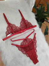 Conjunto de lencería de encaje rojo compuesto por el Bra Olimpia, un corpiño tipo bralette triangular con breteles finos, y la Tanga Bosque, una bombacha tipo tanga con detalles de tiras elásticas decorativas en la cintura.