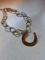 Collar dorado con cadena de eslabones grandes y dije de herradura con detalles de perforaciones.