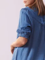Blusa de lyocell color celeste, con cuello a la base, escote en V y botones. Delantera con bolsillo. Manga corta con terminación en punto smock.