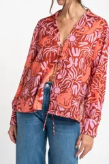 Blusa oversize de poliéster con estampado de animales y plantas en tonos rosa y marrón. Tiene cuello camisero, mangas largas y cierre frontal con lazos.