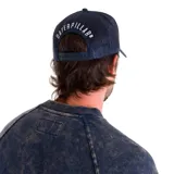 Gorro trucker con visera curva, paneles frontales grises, paneles traseros de malla azul marino y parche frontal con el logo de "Tractor Quality Company".