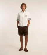 Camisa masculina de algodón con corte boxy, cuello con solapa y rayas, abotonado delantero, bolsillo con estampa floral y estampa trasera de palmera con la palabra 'Paradise'.
