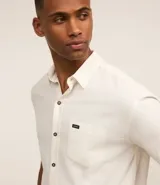 Camisa de hombre de corte relajado, color crudo, con cuello inglés, mangas cortas, abotonado delantero, bolsillo en el pecho y etiqueta de la marca.