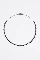 Collar tipo gargantilla con cadena fina de metal oscuro, adornado con una hilera continua de cristales facetados en forma de corazón de color negro.