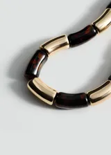 Collar corto con cuentas cilíndricas de resina color carey alternadas con cuentas doradas, unidas por cordón negro ajustable.