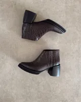 Botín de cuero marrón con estampado de cocodrilo, taco geométrico negro y cierre lateral.