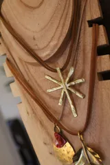 Collar con dije de estrella de bronce con textura martillada, colgando de un cordón doble de cuero sintético marrón.