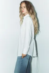 Camisa blanca de corte amplio, con cuello solapa, manga larga y cierre frontal con botones.