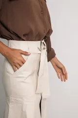 Falda midi color marfil de cuerina, con cierre metálico frontal, cinturón con lazo y abertura delantera.