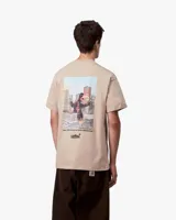 Remera de manga corta color beige, con cuello redondo y un pequeño estampado negro en el pecho izquierdo con texto.