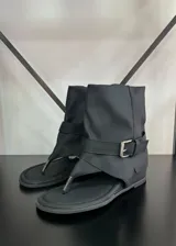 Sandalias negras con diseño de bota corta, tira entre los dedos y hebilla lateral.