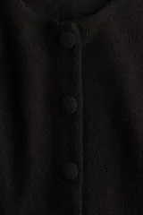 Saco negro en tejido bouclé con cuello redondo, botones forrados hasta la cintura y corte acampanado en la parte inferior.