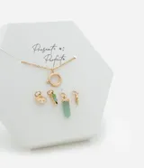 Collar corto dorado con cierre de aro y cuatro dijes colgantes: mano de Fátima, dije con piedras verdes, cristal facetado verde agua y dije con forma abstracta.