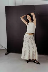Conjunto de top y falda midi de punto color crema con ribetes negros. El top es ajustado, sin mangas y con cuello redondo. La falda es acampanada y con cintura elástica.