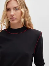 Polera negra de tela rib con cuello alto y mangas largas. Presenta pespuntes rojos en cuello, hombros y puños.