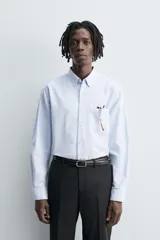 Camisa de algodón color celeste claro, corte regular fit, con cuello abotonado (button-down), manga larga con puño abotonado y bolsillo de parche en el pecho izquierdo.