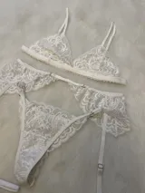 Conjunto de lencería de encaje color bordó, compuesto por un corpiño tipo bralette con breteles regulables, una tanga regulable con corte media less y un portaligas con volados y ligas incluidas.