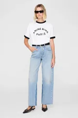 Camiseta blanca de algodón con cuello redondo y mangas cortas con ribete negro. Estampado frontal con la leyenda "ANINE BING PARIS" en letras negras.