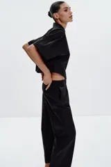 Camisa negra de popelín con cuello solapa y manga ancha por debajo del codo. Detalle de pinzas en la espalda y cierre frontal con botones ocultos por solapa.