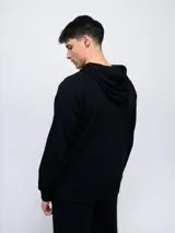 Canguro negro de felpa sin frisa con capucha y logo Umbro bordado en rojo en el pecho. Cuenta con bolsillo tipo canguro y cordones ajustables en la capucha.