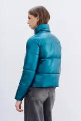 Campera puffer metalizada color azul petróleo, con cuello alto, cierre frontal y bolsillos con cierre. Tiene ajuste interno en el ruedo.