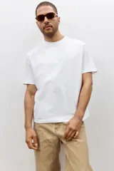 Remera blanca de algodón pesado, corte holgado, con cuello redondo ribeteado, hombros caídos y bajo recto.