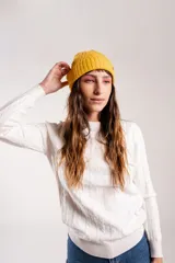 Gorro de lana color amarillo mostaza con detalle de etiqueta con logo en el lateral.