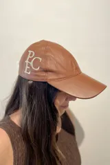Gorra de cuero ovino color camel, confeccionada a mano, con bordado del monograma "PEC" en hilo blanco en el lateral.