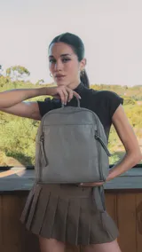 Mochila negra de símil cuero con costuras diagonales en el frente. Tiene un bolsillo frontal con broche magnético, asa de mano y correas regulables.