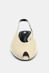 Zapato plano destalonado color beige, con punta abierta, tira trasera con elástico ajustable y suela a contraste de color.